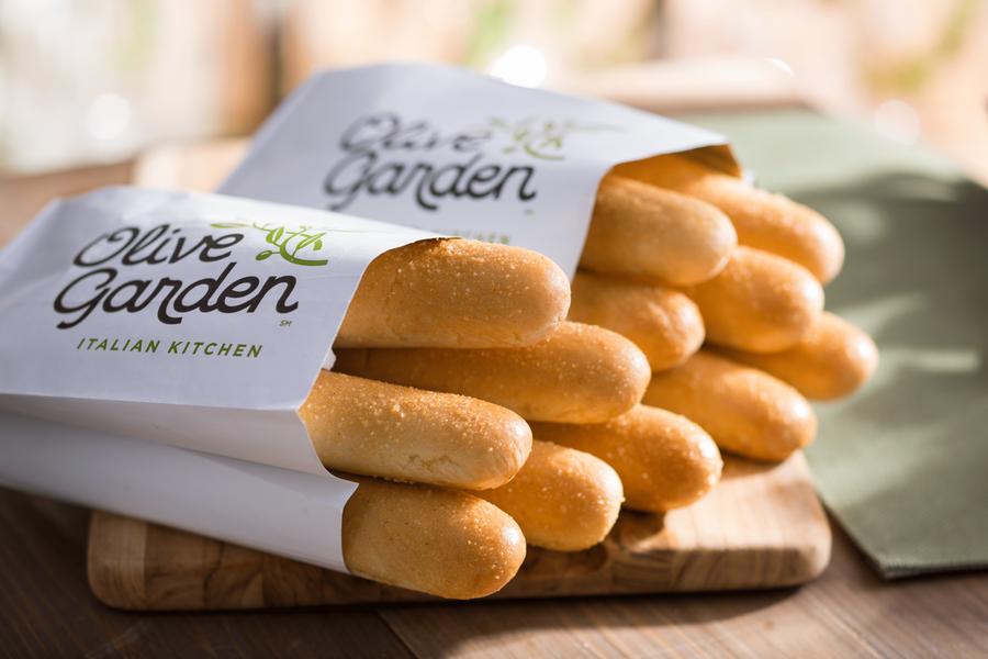 Breadsticks de Olive Garden recién horneados en sus bolsas de papel sobre una tabla de madera