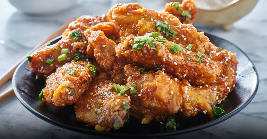 Alitas doradas cubiertas de salsa, servidas en un plato negro