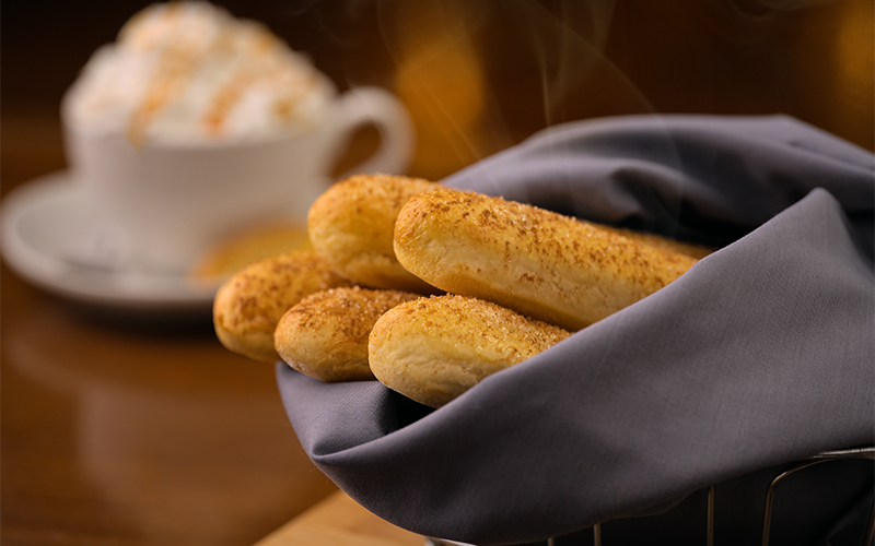 Panoli dulces dorados servidos en una servilleta junto a una taza de café con crema