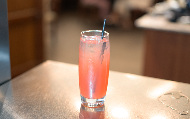 Cóctel Bay Breeze rosado con hielo y pajilla sobre la barra