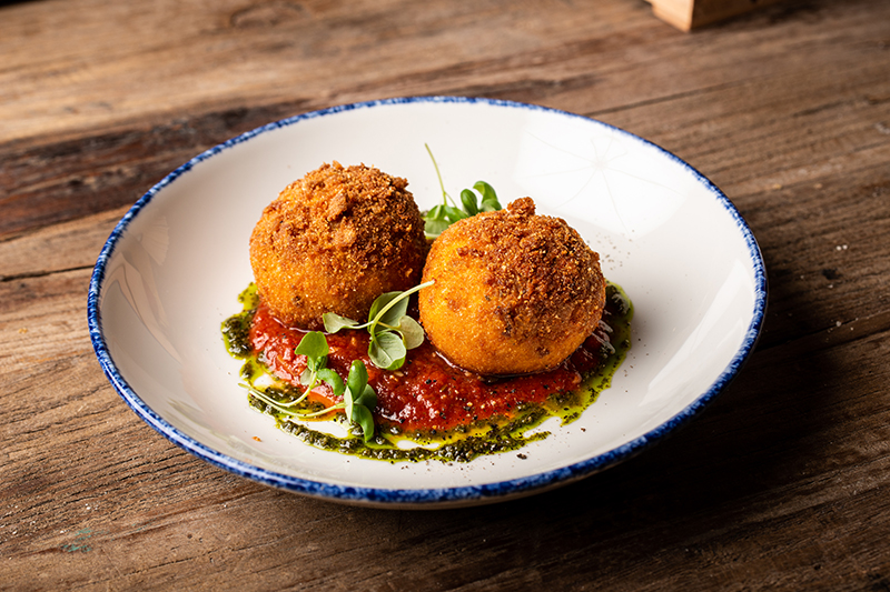 Dos arancini di ossobuco de Lucca sobre salsa de tomate y pesto
